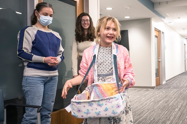 Berlin Duellman, a 6-year old with cerebral palsy, tries out a device that will help her carry items while her mother, Laural (far left), and McKelvey Engineering student Grace Huntington look on. (Photo: Carol Green/Washington University)