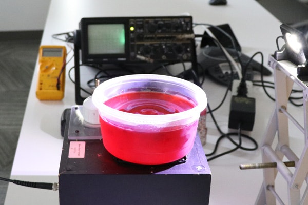 Ruth Okamoto uses a bowl of gelatin on a speaker as a model for the brain’s motion when the skull experiences vibrations. (Photo: Brook Haley/Washington University)